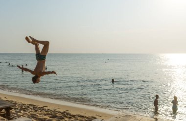 Spor faaliyetleri n plaj. Backflip günbatımı, jimnastik akrobatik blanche, motivasyon içerikli spor exersices yapan genç erkek ile güzel sahilde plaj