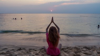 Sahilde günbatımı güzel manzaralı denizde sakin dalgalar ile izlerken yoga kavramı ile oturan uzun kızıl saçlı kız seyahat
