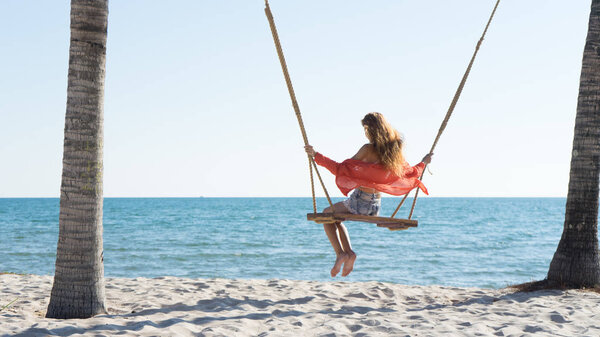 Концепция отпуска. Молодая женщина качается на пляжных качелях. Счастливые путешественницы на пляже Фу Куок
