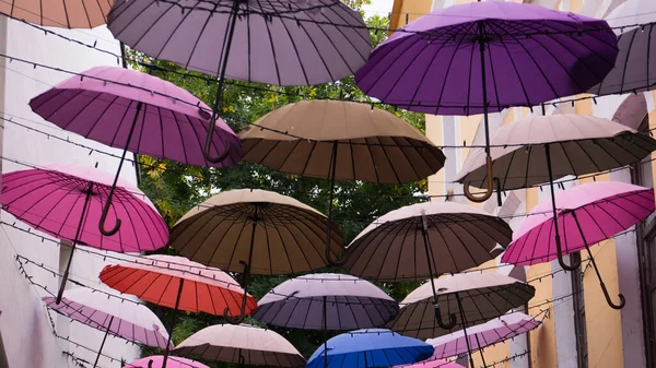 城市街道上五颜六色的雨伞装饰的背景 五颜六色的雨伞挂在古老街道上的甲虫中间 免版税图库照片