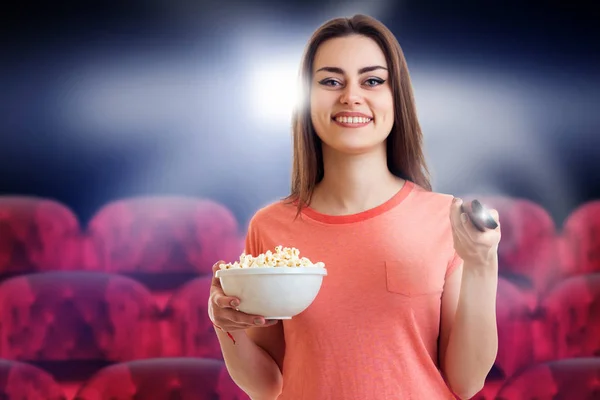 Cute young girl watch movie with pop-corn and smiles at the cinema