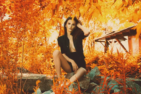 秋の公園で岩に座っている黒のスーツで官能的な美少女 — ストック写真