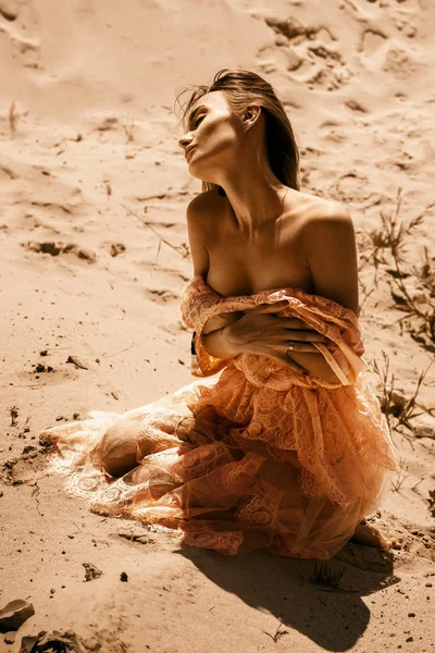 gorgeous lady wth closed eyes in pink dress sits in a hot desert