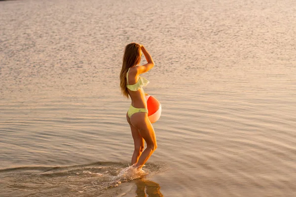可爱的苗条的夫人泳装与海滩球在海在温暖的日落 — 图库照片