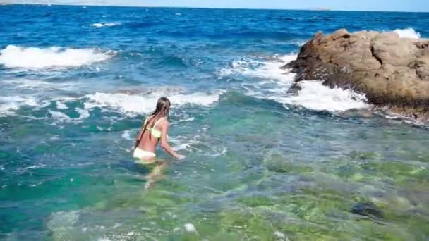 Jong meisje zwemt in het wild rotsachtige strand — Stockvideo