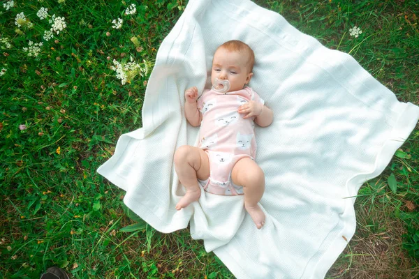 小さな女の赤ちゃんは緑の草の上に白い毛布の上に横たわっています — ストック写真