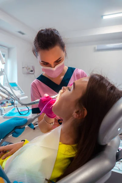 Dentista de uniforme rosa tratar os dentes de um paciente — Fotografia de Stock