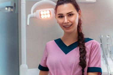Pembe üniformalı güzel dişçi kamerada gülümsüyor.