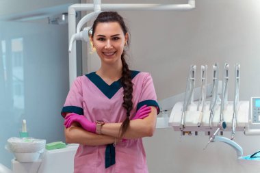 Pembe üniformalı güzel dişçi klinikteki kamerada gülümsüyor.