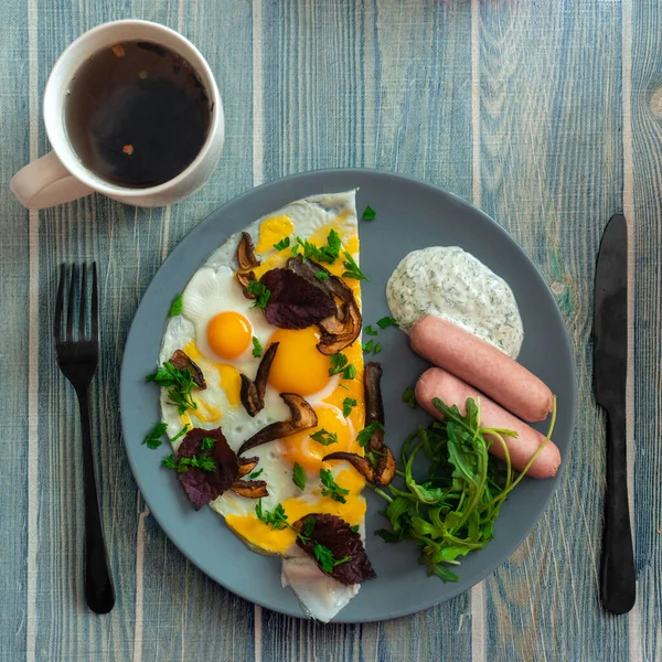 square picture of breakfast eggs with sausages and mushrooms on the plate