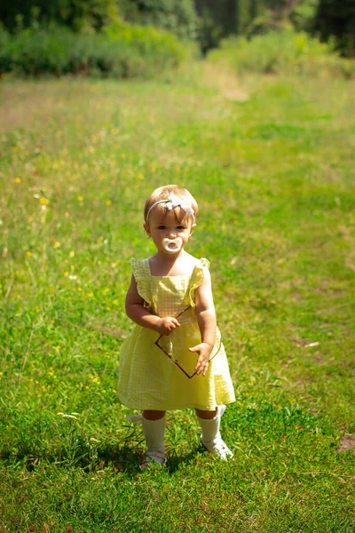 Cute little girl dziecko w żółtej sukience patrząc na aparat w ogrodzie — Zdjęcie stockowe