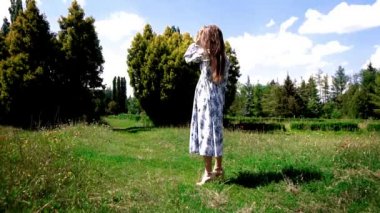 Çekici kadın yeşil bahçede uzun elbiseler içinde yürüyor.