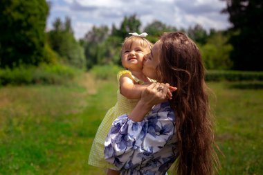 Sevimli genç anne yeşil parkta küçük kızını öpüyor.