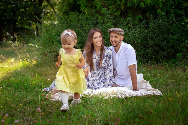 Linda niña en vestido amarillo corriendo a sus padres. Padre y madre mirando a su hija y sonríe en el picnic — Foto de Stock