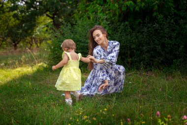 Neşeli, şık, genç anne küçük kızıyla yeşil bahçede oynuyor.