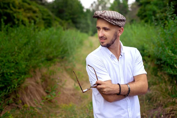 Elegantní Muž Klobouku Drží Sluneční Brýle Dívá Stranou Zelený Park — Stock fotografie