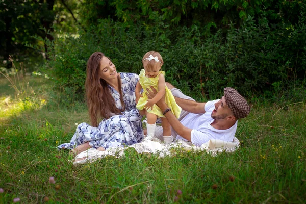 Retrato de alegre joven familia juega con su liitle bebé hija en el prado grren — Foto de Stock