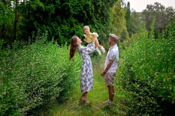 Fröhliche junge Eltern spielen mit ihrem kleinen Mädchen im grünen Garten — Stockfoto