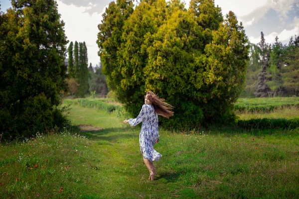 Fröhliche brünette Frau auf Stöckelschuhen spaziert in langem Kleid mit Blumen-Print im Freien — Stockfoto