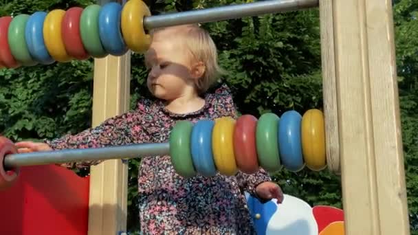 Hermosa niña juega con círculos multicolor en un patio de recreo — Vídeos de Stock