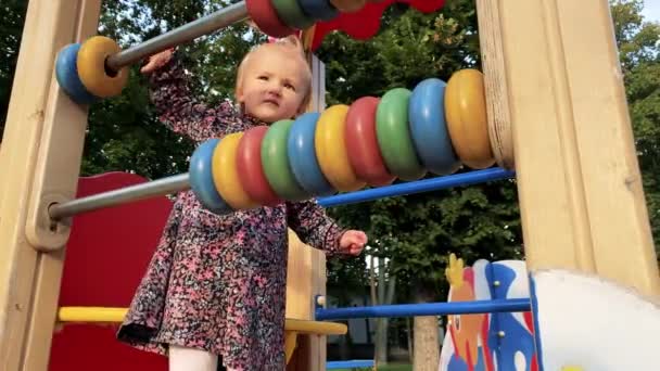 Hermosa niña juega con círculos multicolor en un patio de recreo — Vídeos de Stock