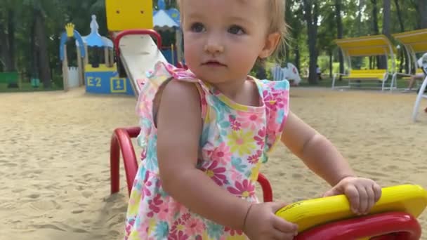 Bonito loira criança menina no vestido com flor imprimir joga em um playground — Vídeo de Stock