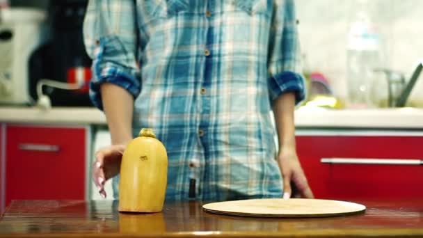 女性はキッチンでまな板に黄色のカボチャの作品を置きます — ストック動画