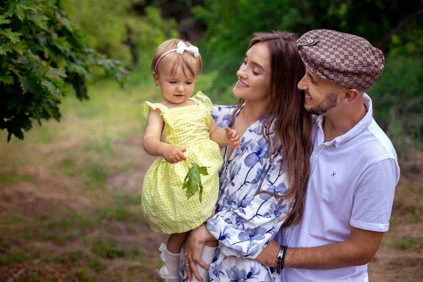 Nahaufnahme Porträt einer schönen jungen Familie, die ein kleines stilvolles Mädchen im grünen Park trägt — Stockfoto