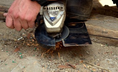 Bir adam açısal öğütme makinesiyle çalışır, kıvılcımlar her yöne uçar.