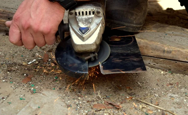 Bir adam açısal öğütme makinesiyle çalışır, kıvılcımlar her yöne uçar.