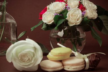 Sessiz tonlarda kahvaltı. Koyu bir arka plan üzerinde bir vazo çikolata şeker kurabiye beyaz ve kırmızı güller