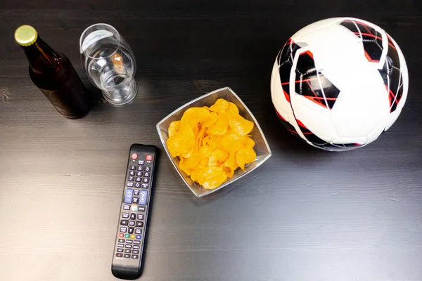 People prepared to watch football on TV with beer. There\'s beer on the table, ball, TV remote, snacks. Craft beer. Light background. The view from the top.