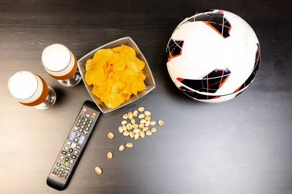 People prepared to watch football on TV with beer. There\'s beer on the table, ball, TV remote, snacks. Craft beer. Light background. The view from the top.