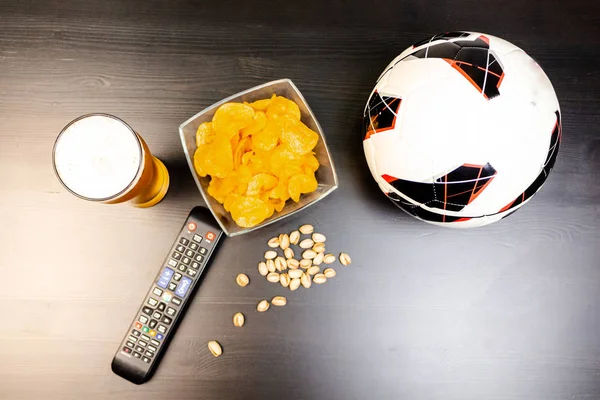 People prepared to watch football on TV with beer. There\'s beer on the table, ball, TV remote, snacks. Craft beer. Light background. The view from the top.