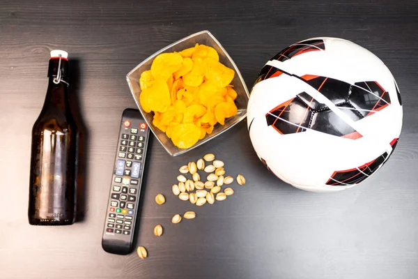 People prepared to watch football on TV with beer. There\'s beer on the table, ball, TV remote, snacks. Craft beer. Light background. The view from the top.