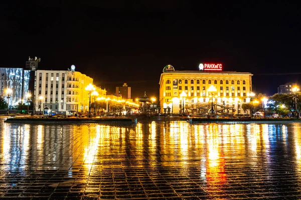 Gece şehri manzarası. Khabarovsk şehrinin ana meydanı fenerlerin ışığında, yağmur henüz geçtikten sonra su birikintilerine yansıyor..