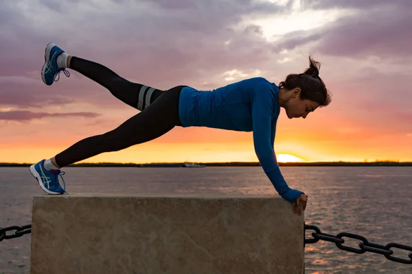 An attractive woman in sports clothes doing sports exercises in nature against the sunset and the Amur river, loves gymnastics, kneads her legs. Active young girl engaged in sports, leads a healthy lifestyle.