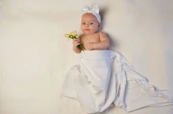 Bella bambina che tiene un fiore sulla coperta bianca — Foto Stock