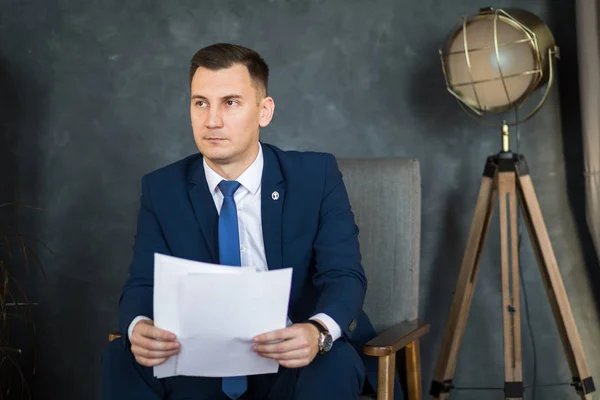 Confident man lawyer in formal wear reading paper documents while sitting in modern office space interior, young handsome male economist studying dossier files before an important meeting with partner