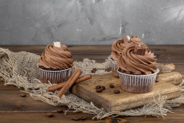 ahşap arka plan üzerinde kakao krema, tarçın ve kahve ile kahverengi cupcakes