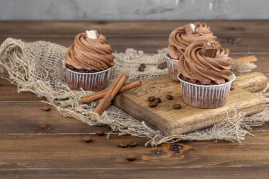 ahşap arka plan üzerinde kakao krema, tarçın ve kahve ile kahverengi cupcakes