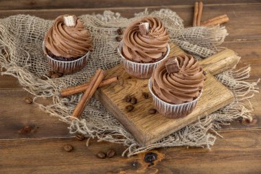 ahşap arka plan üzerinde kakao krema, tarçın ve kahve ile kahverengi cupcakes