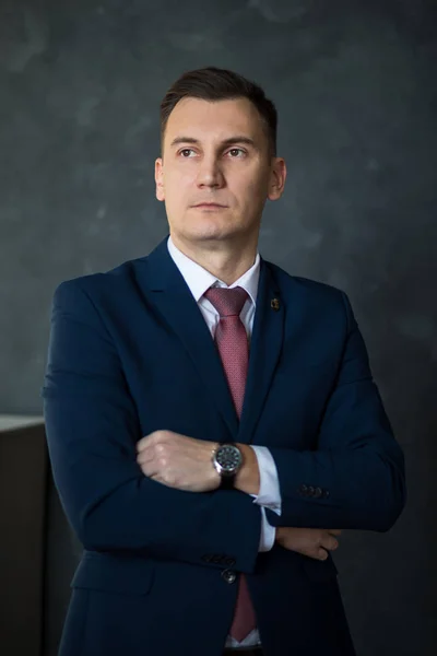 Portrait of young intelligent man lawyer standing with crossed arms in modern office building interior, successful male bank employee dressed in luxury suit posing with copy space area for your text