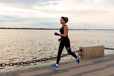 Khabarovsk, Rusya - 07 Ekim 2018: Genç ve çekici bir kız bir şehir Parkı'nda gün batımında koşuyor. Sağlıklı fitness kadın açık havada çalışan. Arka planda Habarovsk ufukta Amur nehri.