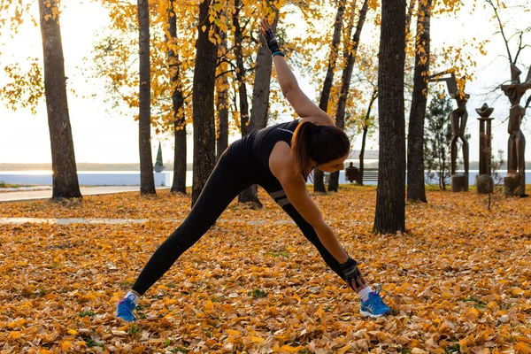 Khabarovsk, Russia - 07 ottobre 2018: Una donna attraente in abiti sportivi che fa esercizi sportivi in natura contro il tramonto e il fiume Amur, ama la ginnastica, impasta le gambe. Attivo giovane ragazza it — Foto Stock