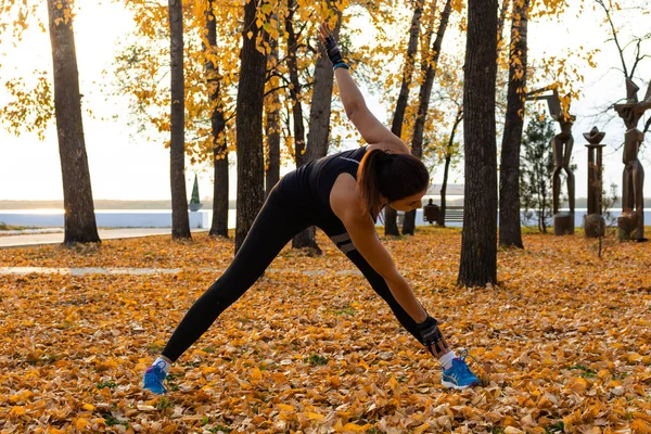 Khabarovsk, Russia - Oct 07, 2018: An attractive woman in sports clothes doing sports exercises in nature against the sunset and the Amur river, loves gymnastics, kneads her legs. Active young girl en — Stock Photo, Image