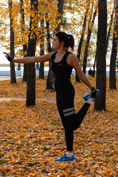 Chabarowsk, Rosja-paź 07, 2018: atrakcyjna kobieta w ubraniach sportowych wykonywania ćwiczeń sportowych w przyrodzie przed zachodem słońca i rzeki Amur, kocha gimnastyka, ugniata nogi. Aktywna młoda dziewczyna pl — Zdjęcie stockowe