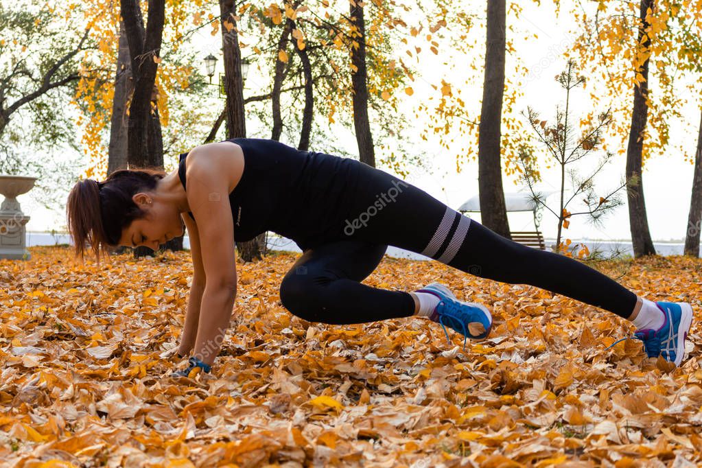 Khabarovsk, Russia - Oct 07, 2018: An attractive woman in sports clothes doing sports exercises in nature against the sunset and the Amur river, loves gymnastics, kneads her legs. Active young girl en