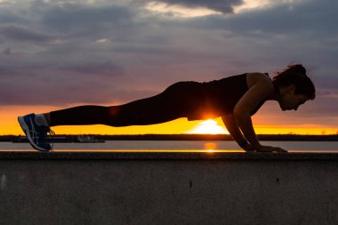 Khabarovsk, Rusya - Eki 07, 2018: Gün batımı ve Amur nehrine karşı doğada spor egzersizleri yapan spor kıyafetleri içinde çekici bir kadın, jimnastiği seviyor, bacaklarını yoğurunuyor. Aktif genç kız tr