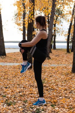Khabarovsk, Rusya - 07 Ekim 2018: Genç sporcu esneme ve koşmaya hazırlanıyor. Doğada spor egzersizleri yapan spor kıyafetleri içinde çekici kadın, sonbahar yapraklarının halısında, jimnastikçi seviyor